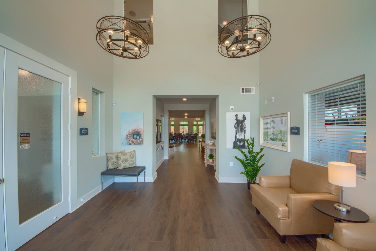 A modern lobby featuring stylish chandeliers, a seating area, and a wooden floor leading into a hallway.