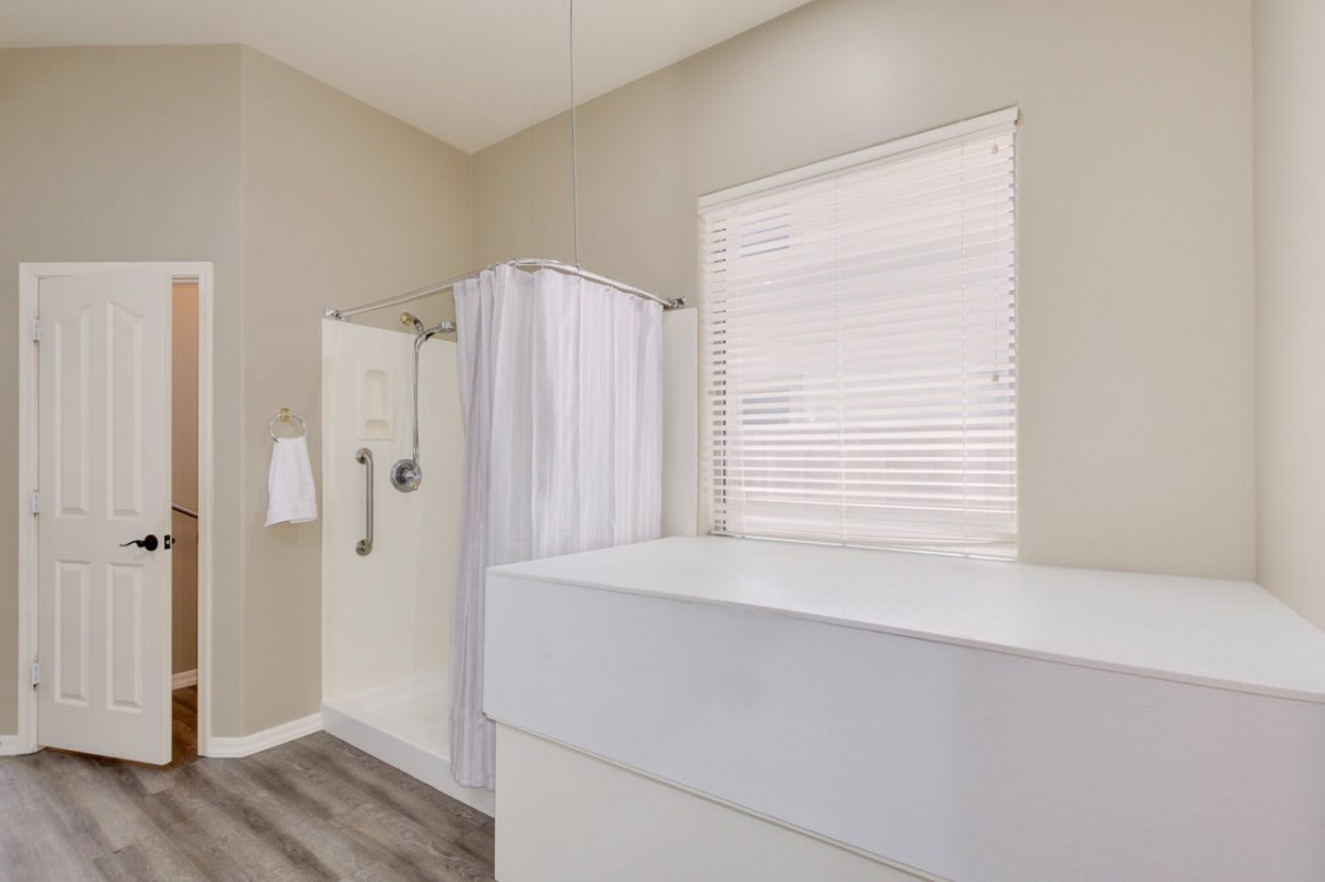 A modern bathroom featuring a shower with a white curtain, a large sink, and a window with blinds.