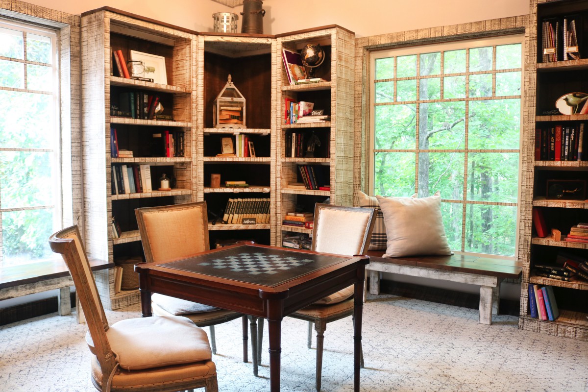 A cozy library corner with bookshelves, a chess table, and a window seat.
