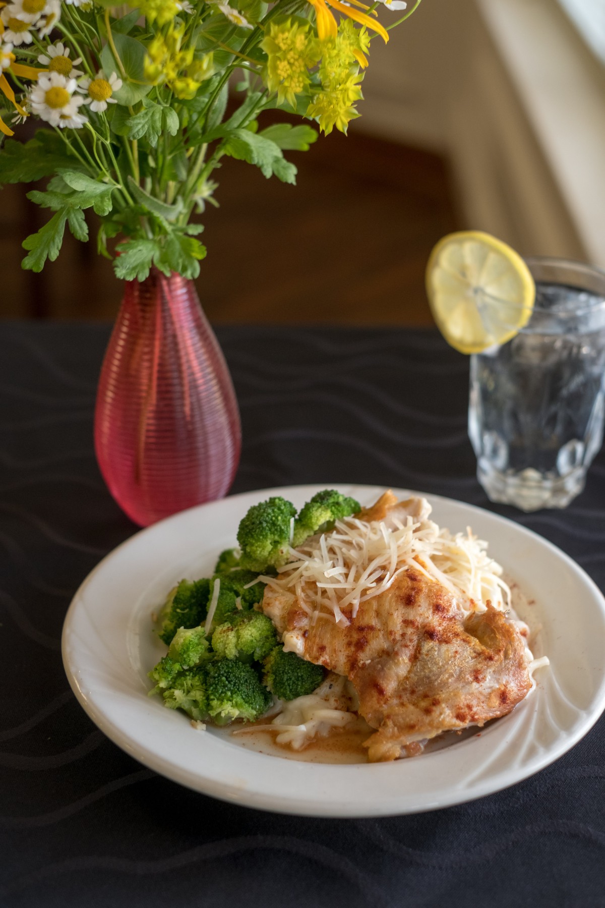 A delicious pasta dish served with broccoli, accompanied by a refreshing glass of lemon water.