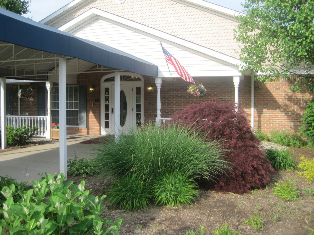 A building entrance with a porch, an American flag, and landscaped greenery.