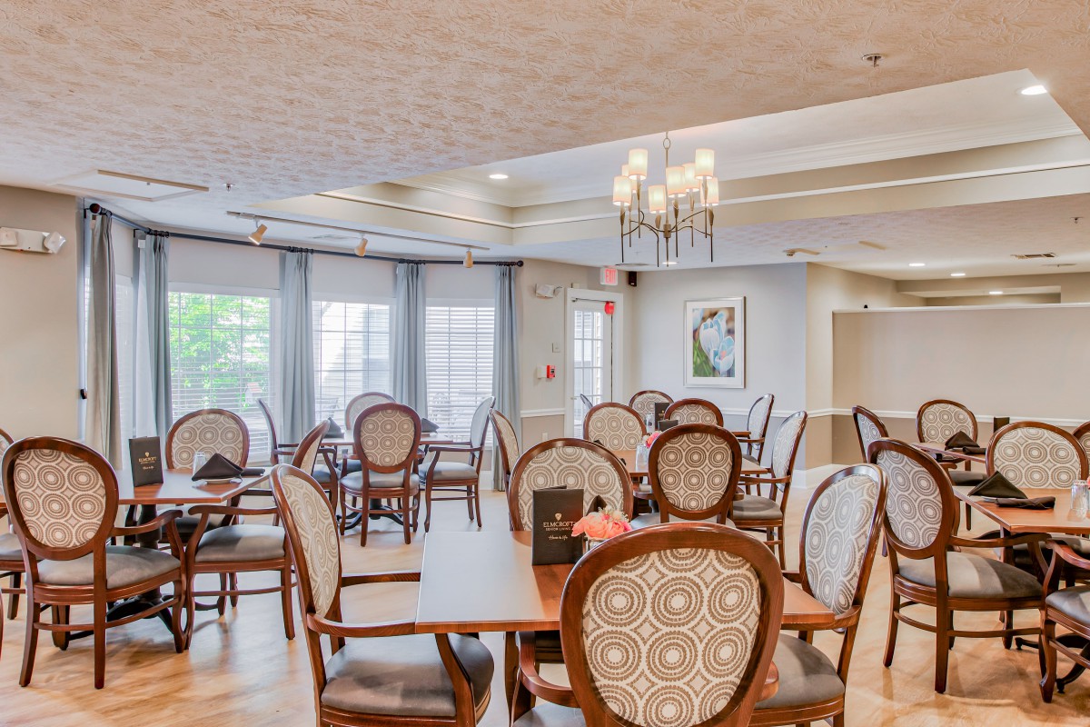 An elegant dining area with classic wooden chairs, a chandelier, and large windows letting in natural light.