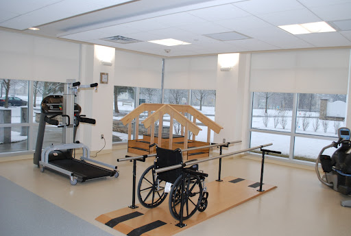A rehabilitation therapy room featuring a wheelchair, wooden balance training structure, and physical therapy equipment.