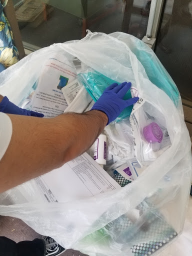 A gloved hand sifting through a bag filled with medical waste and disposable items.