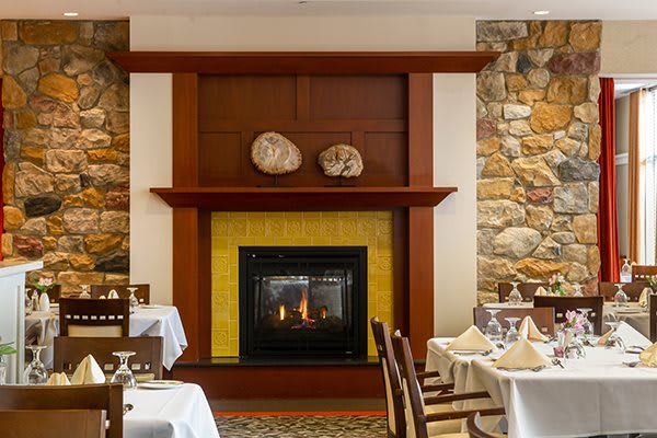 A cozy restaurant dining area featuring a central fireplace and elegantly set tables.