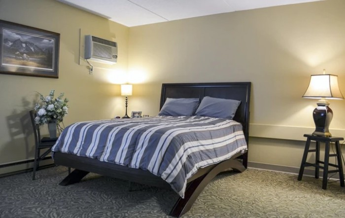 A cozy bedroom with a striped bedspread and wall-mounted air conditioner.