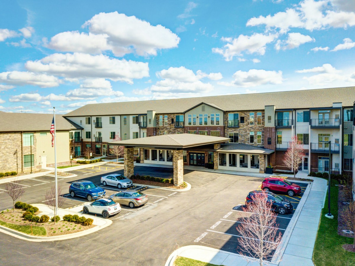 A large building with a parking lot filled with cars under a partly cloudy sky.