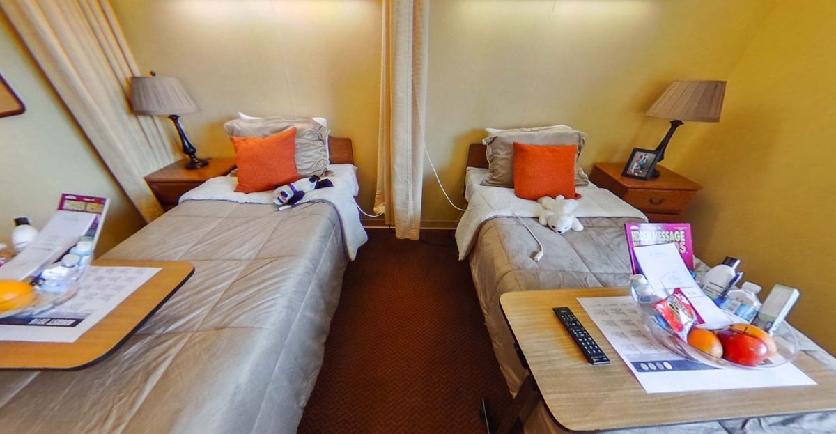 A cozy hotel room with twin beds and orange accent pillows.