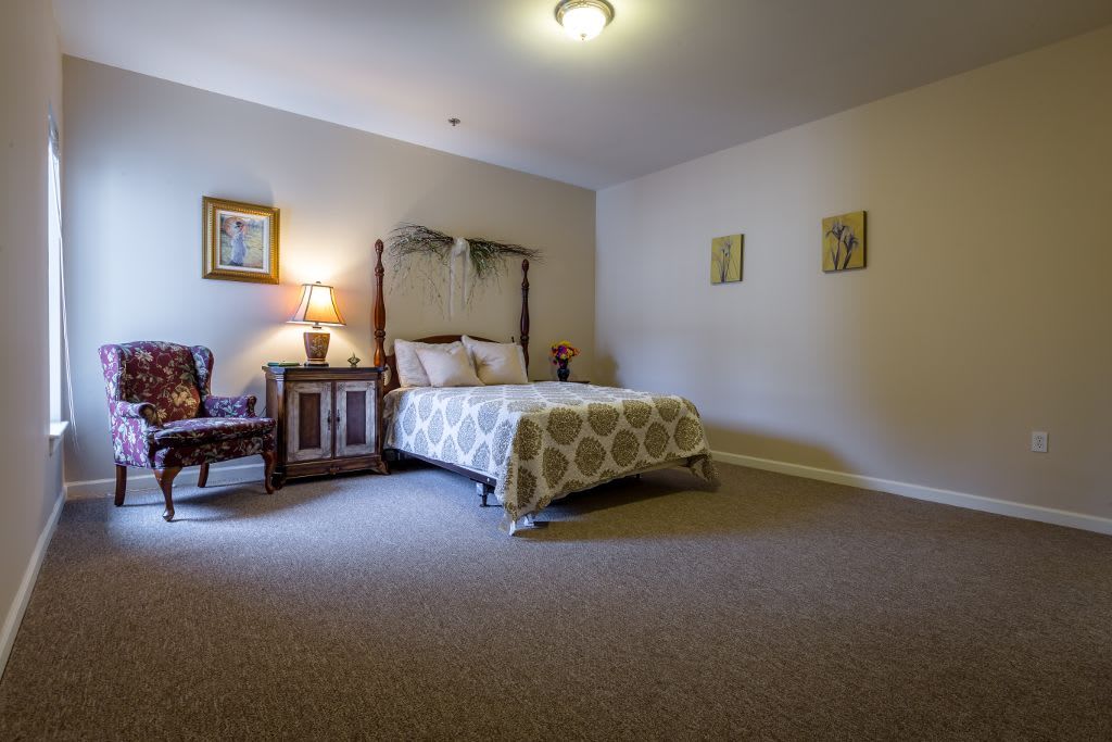 A cozy bedroom featuring a bed with patterned bedding, a wooden nightstand with a lamp, and decorative wall art.