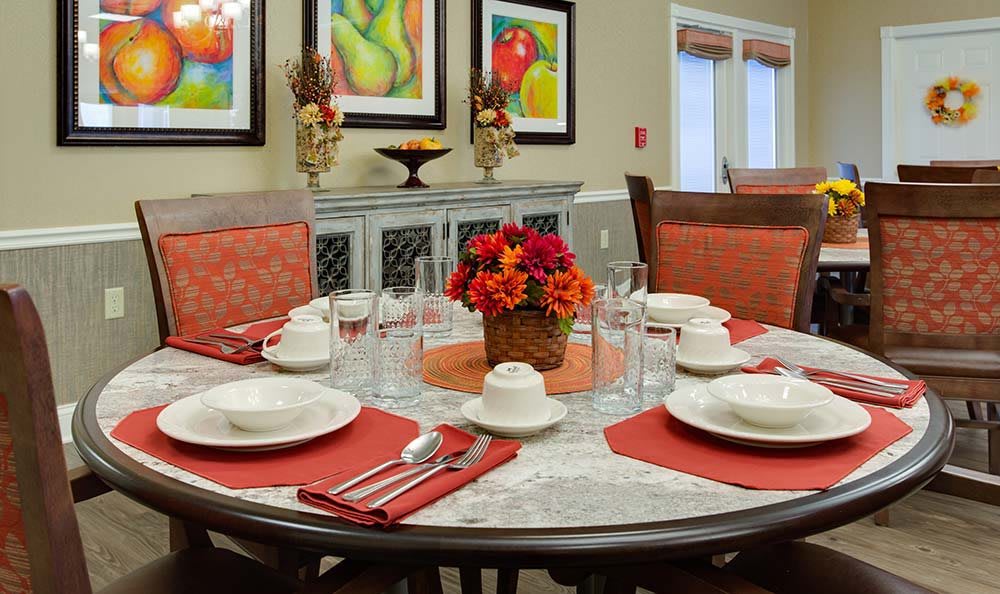 A dining table elegantly set for four, adorned with vibrant flowers and surrounded by colorful artwork.
