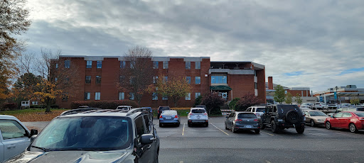 A view of an apartment complex with a parking lot full of cars under a cloudy sky.