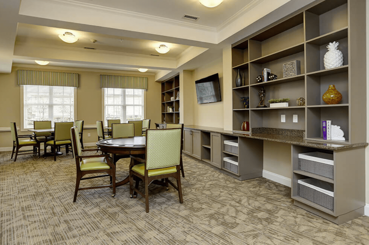 A well-lit dining area with a round table and chairs, surrounded by built-in library shelves and a mounted television.