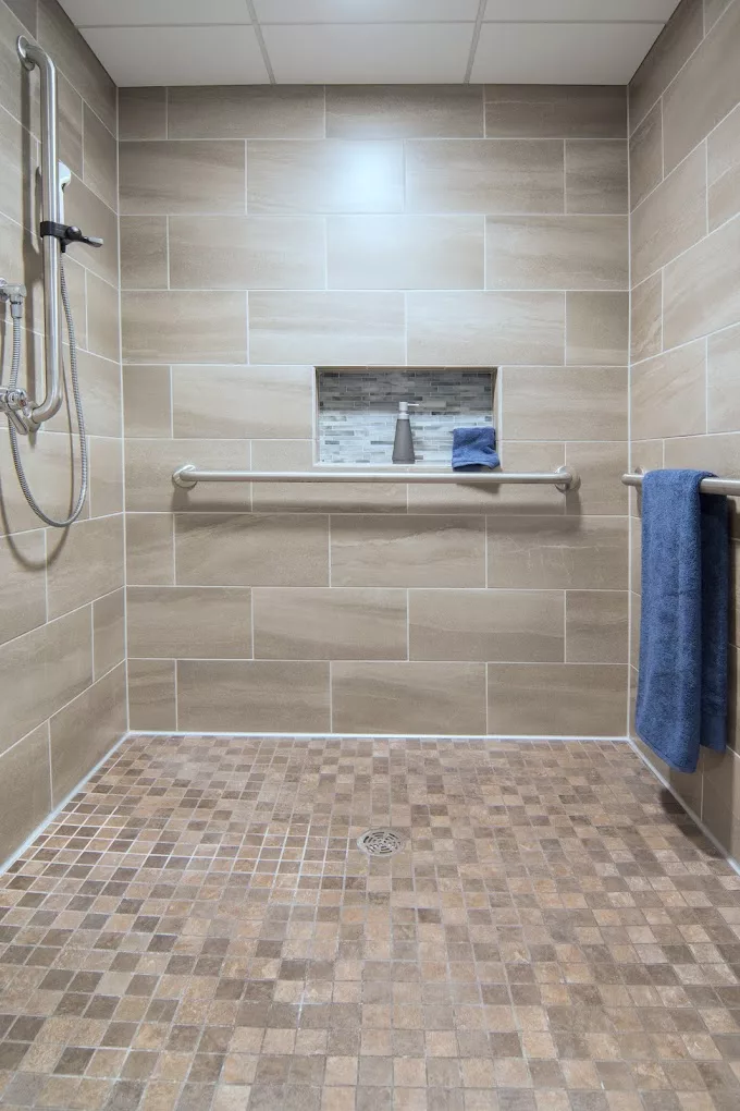 A modern walk-in shower featuring beige wall tiles, a niche shelf with toiletries, and a blue towel on a towel rack.