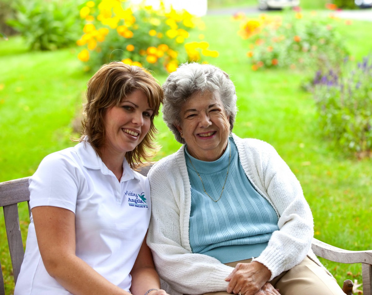 A younger woman and an elderly woman smiling together in a garden.
