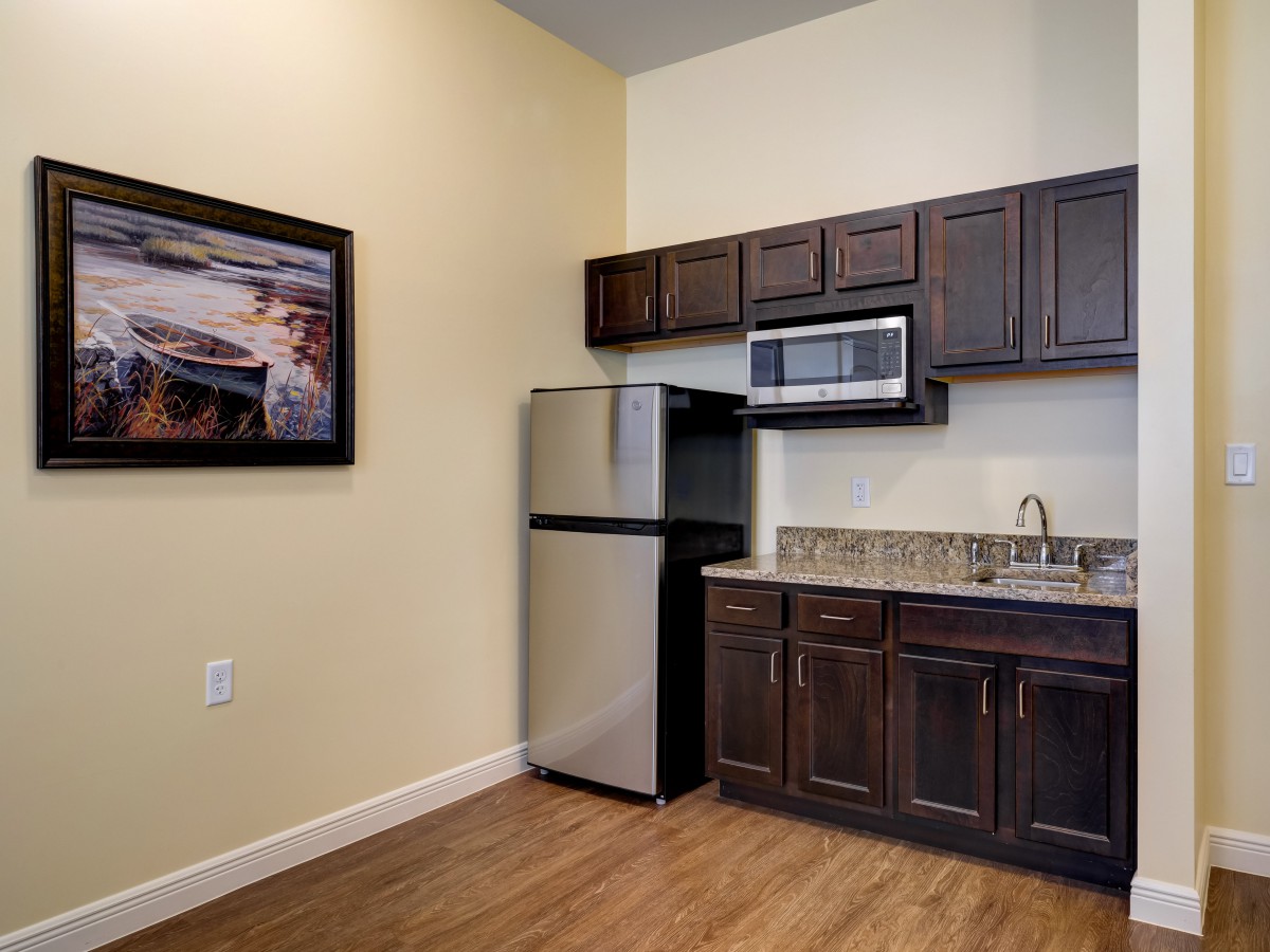 A compact kitchen area with dark wood cabinets, stainless steel refrigerator and microwave, and a small countertop and sink.