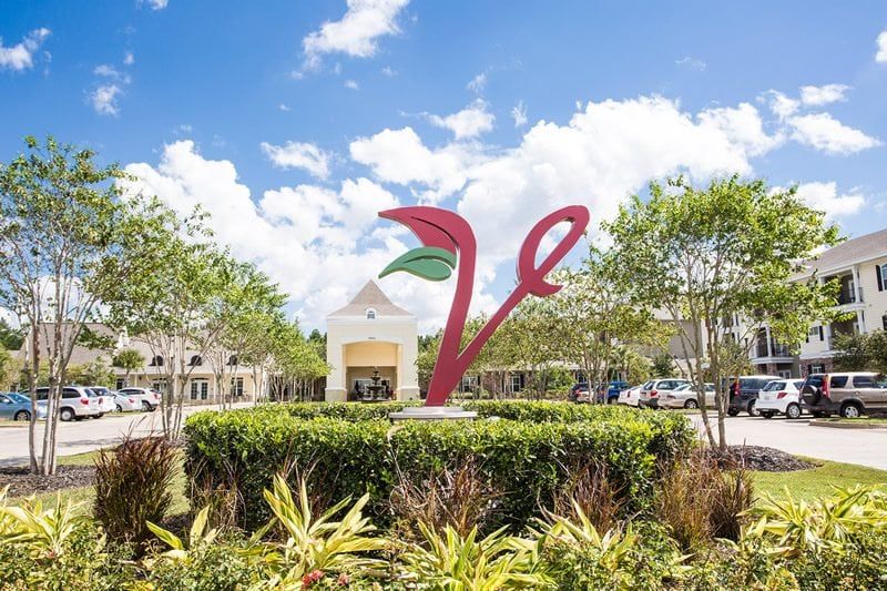 A vibrant sculpture stands in front of a shopping center, surrounded by lush greenery under a clear blue sky.