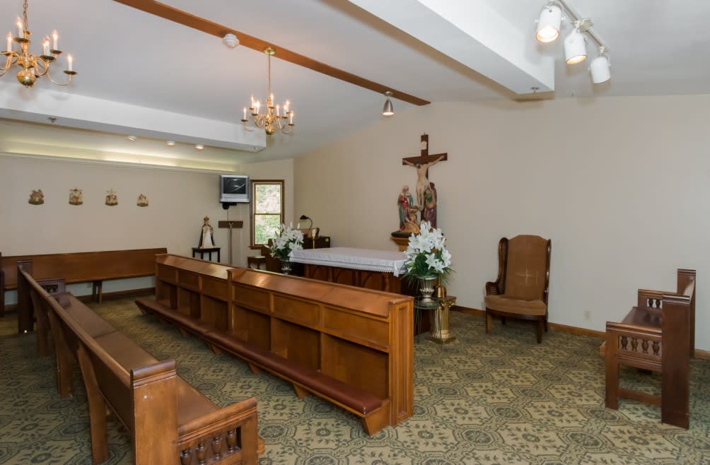 A small chapel interior featuring an altar with a crucifix and statue, surrounded by benches.