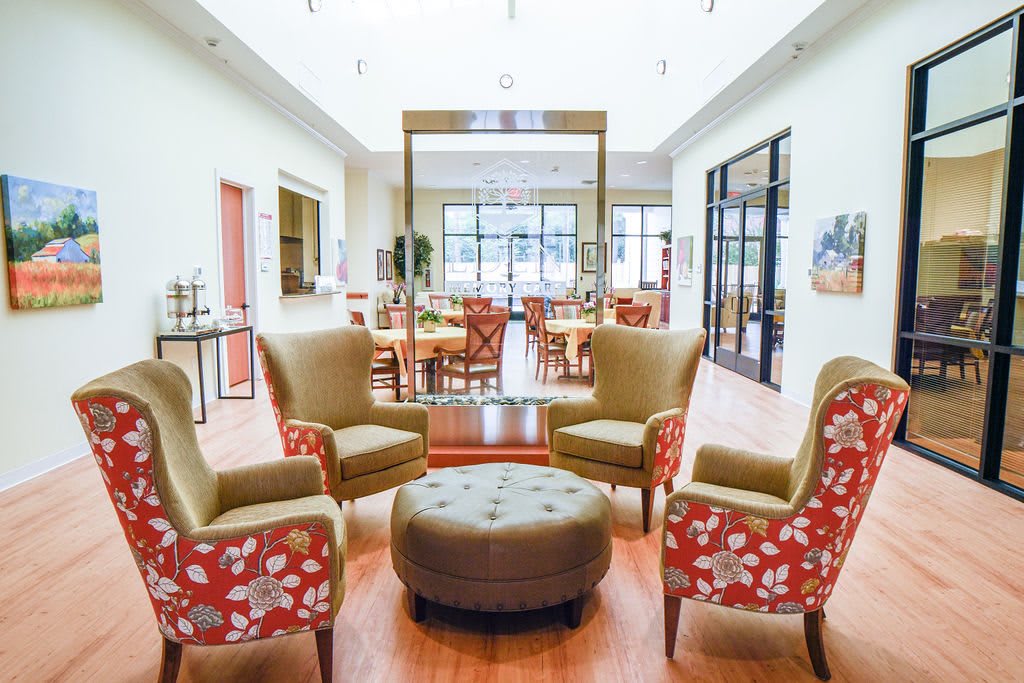 A spacious and elegant seating area with four chairs around an ottoman, leading into a bright dining space.