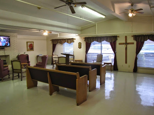 A serene interior of a chapel with wooden seating and a prominent cross on the wall.