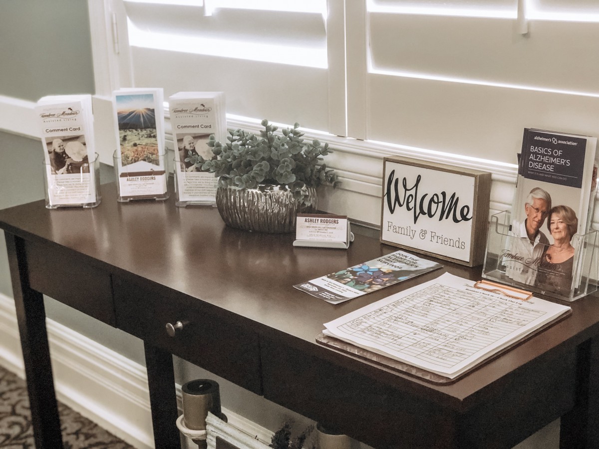 A neatly organized desk with a welcome sign, brochures, a calendar, and an indoor plant.