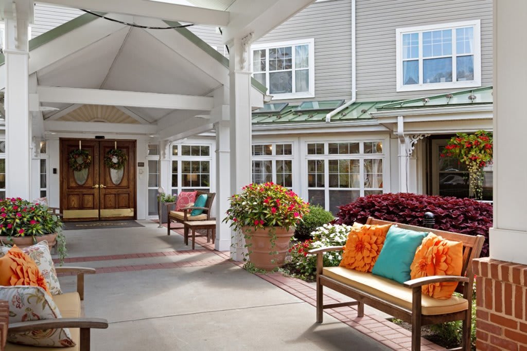 A welcoming building entrance with benches adorned with colorful cushions and vibrant potted flowers.