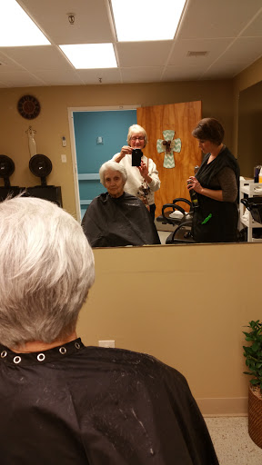 A senior woman receives a haircut at the salon, while stylists assist her in front of a mirror.