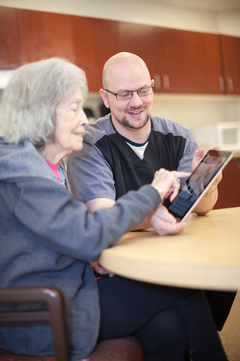A caregiver assists an elderly woman as they explore a tablet together, sharing a moment of connection and learning.