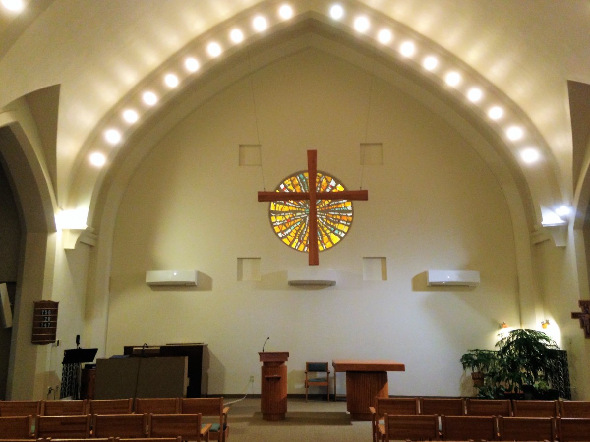 Interior of a church sanctuary featuring a cross and stained glass window.
