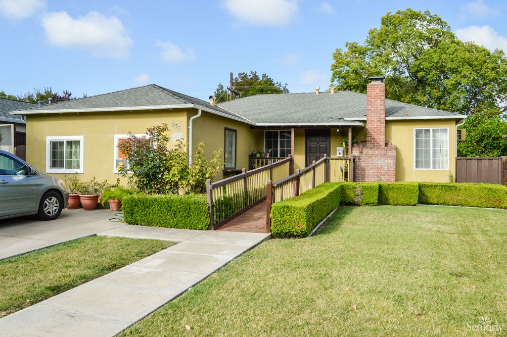 A suburban house with a ramp leading to the entrance, surrounded by a well-maintained lawn and garden.