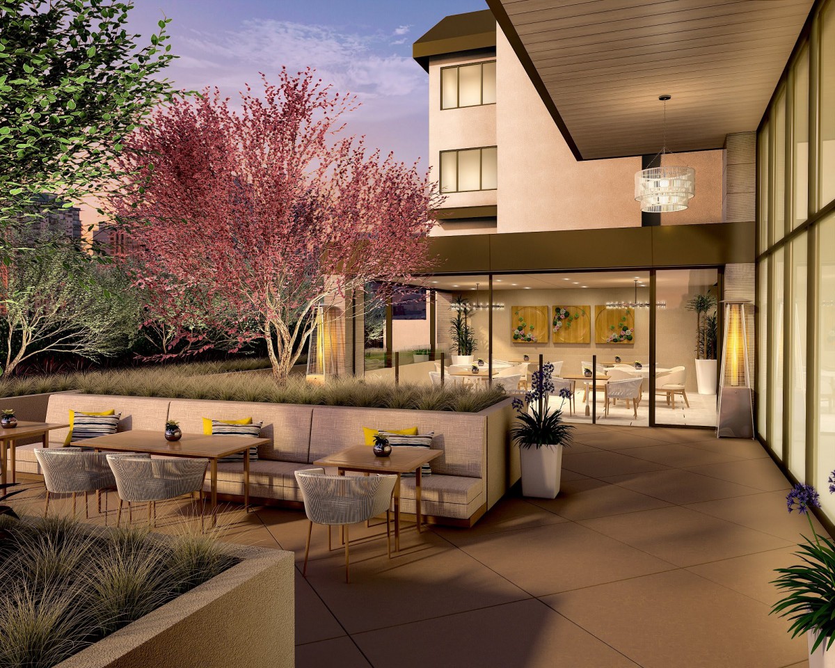 A modern restaurant patio with outdoor seating, set against a backdrop of trees during the evening.