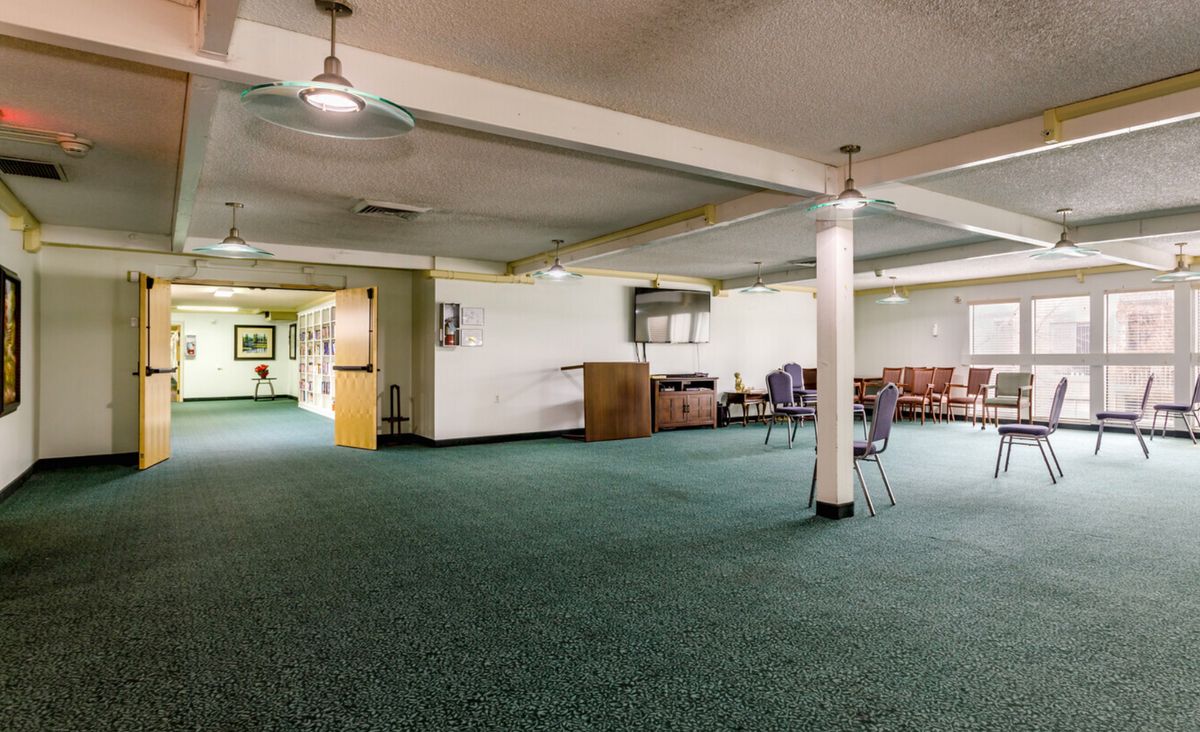 A spacious basement room with green carpet, pillars, and scattered furniture.