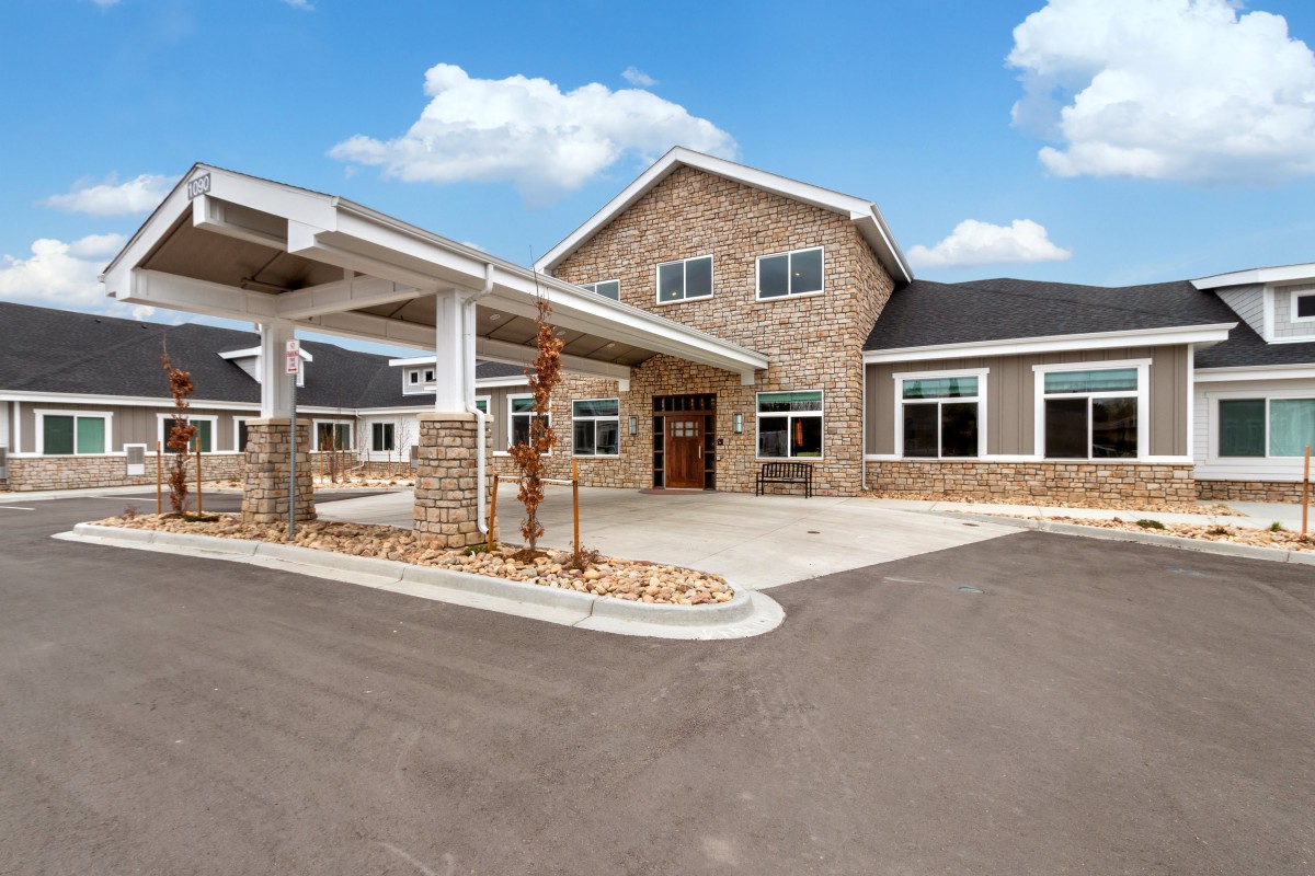 A modern residential building with a stone facade and a spacious driveway under a clear blue sky.