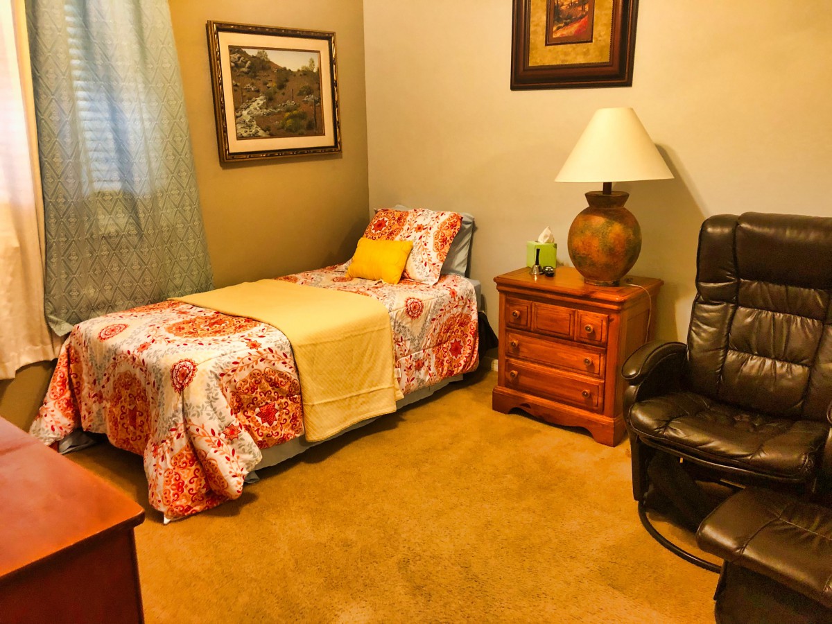 A cozy bedroom with a single bed, nightstand, and comfortable chair.