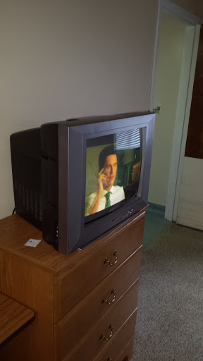 A vintage television set displaying a scene, placed on a wooden dresser in a cozy room.