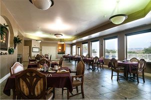 A spacious dining room with neatly arranged tables and chairs, large windows, and ambient lighting.