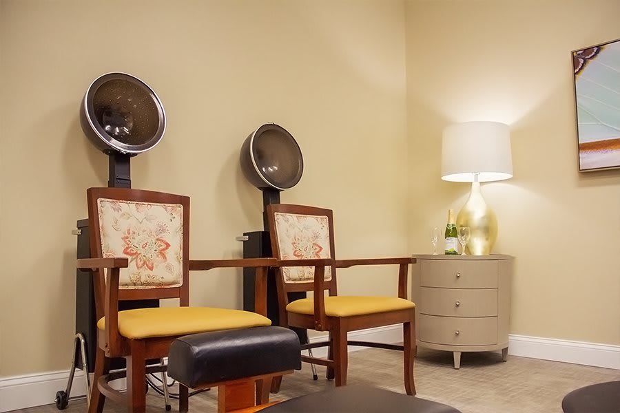 A cozy salon interior with chairs and built-in hair dryers, complemented by a lamp and side table.
