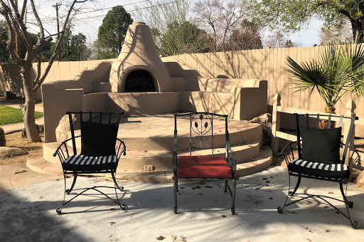 A cozy outdoor seating area featuring three chairs around a charming fireplace.