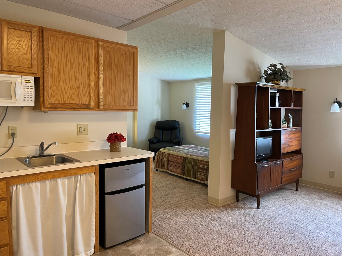 A cozy studio apartment featuring a kitchenette, living area, and bedroom space.