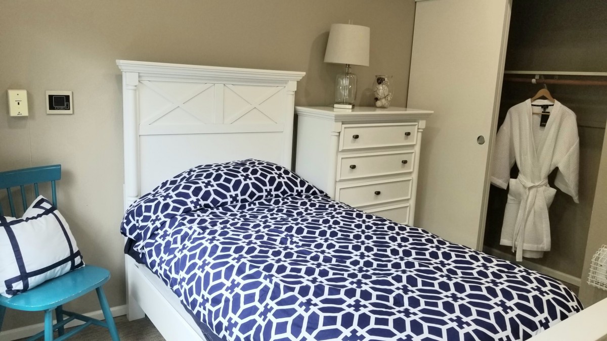 A neatly arranged bedroom featuring a white bed with patterned bedding and a matching dresser with a lamp.