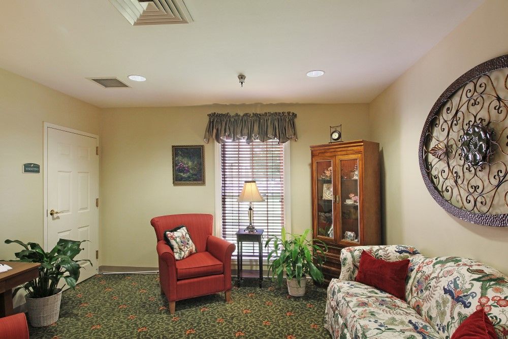A cozy living room with a red armchair, decorative cushions, a cabinet, and a lamp beside a window with curtains.