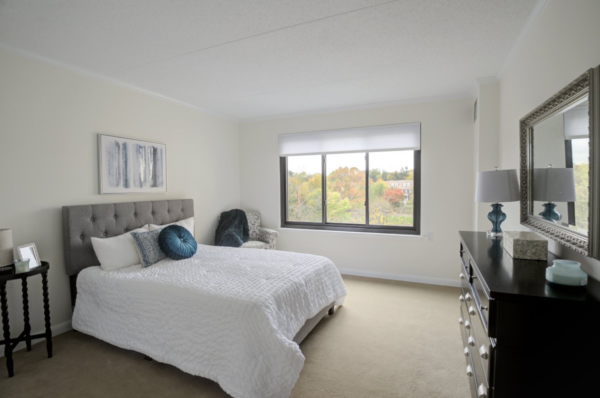A bright and cozy bedroom with a large window, a neatly made bed, and simple decor.