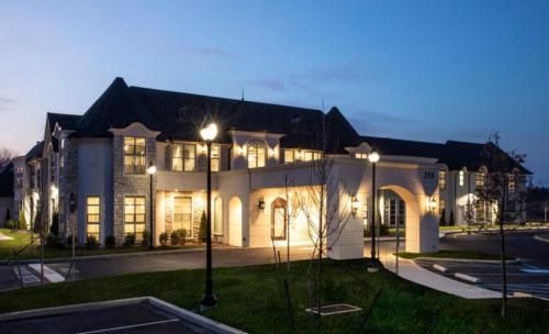 Luxury mansion lit up at dusk with a spacious driveway.