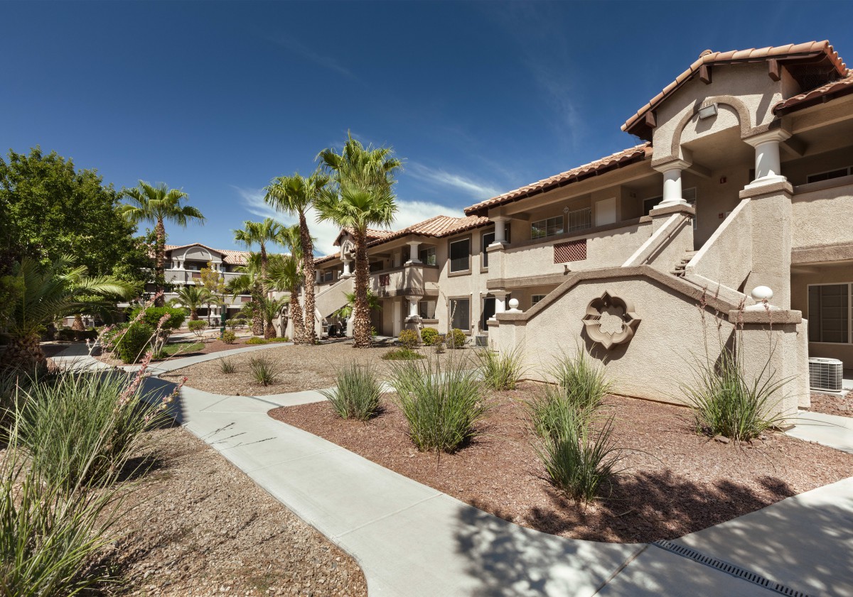 A southwestern-style apartment complex with palm trees and a desert landscape under a clear blue sky.