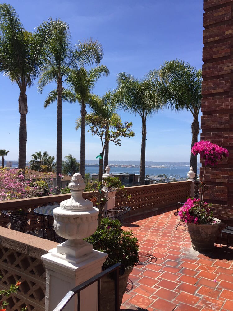 A scenic view from a brick patio overlooking the ocean, adorned with palm trees and vibrant bougainvillea.