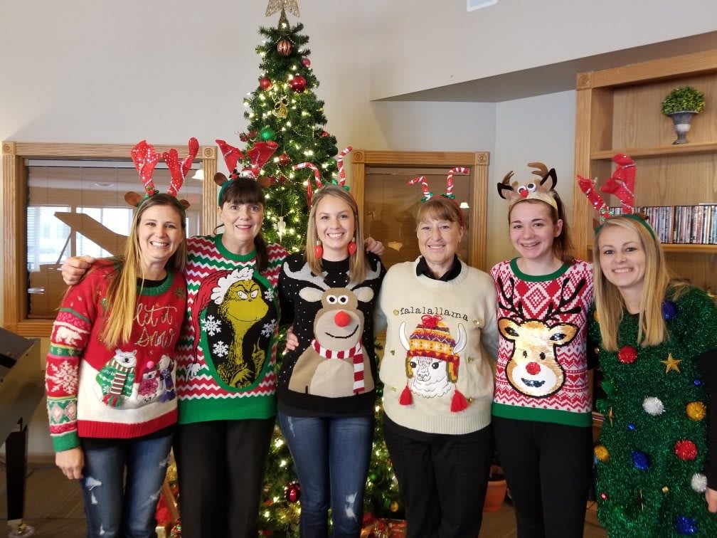 A group of people wearing festive Christmas sweaters standing in front of a decorated tree.