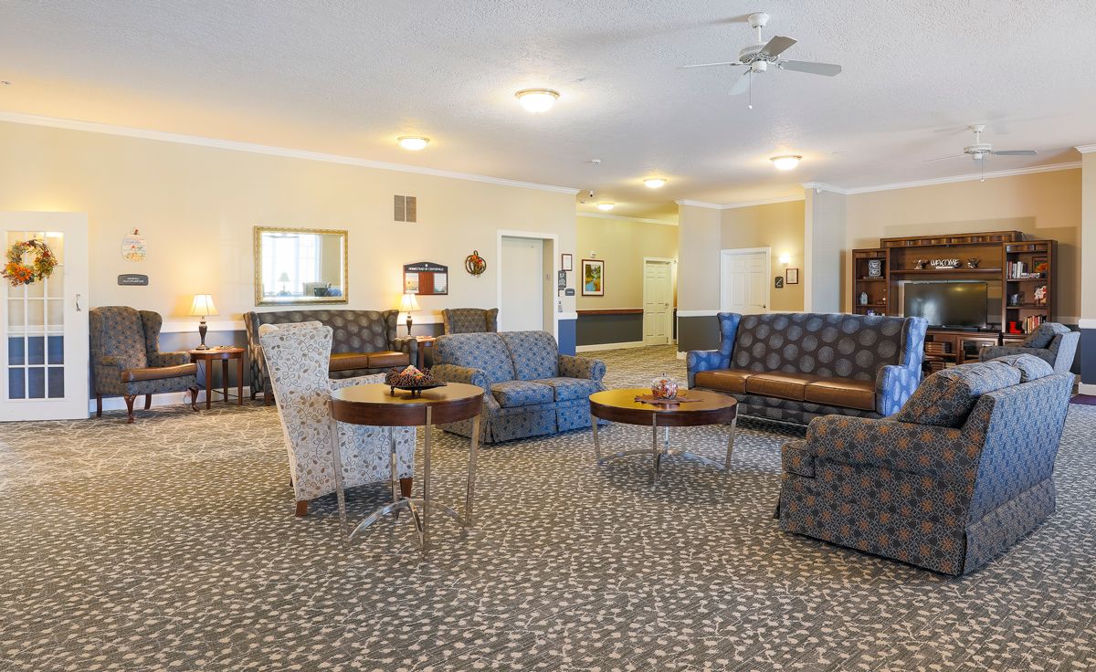 A spacious living room featuring multiple seating arrangements with sofas and round tables on a carpeted floor.
