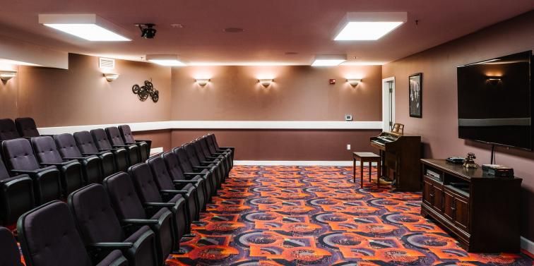 An empty theater room with rows of black chairs and colorful carpet.