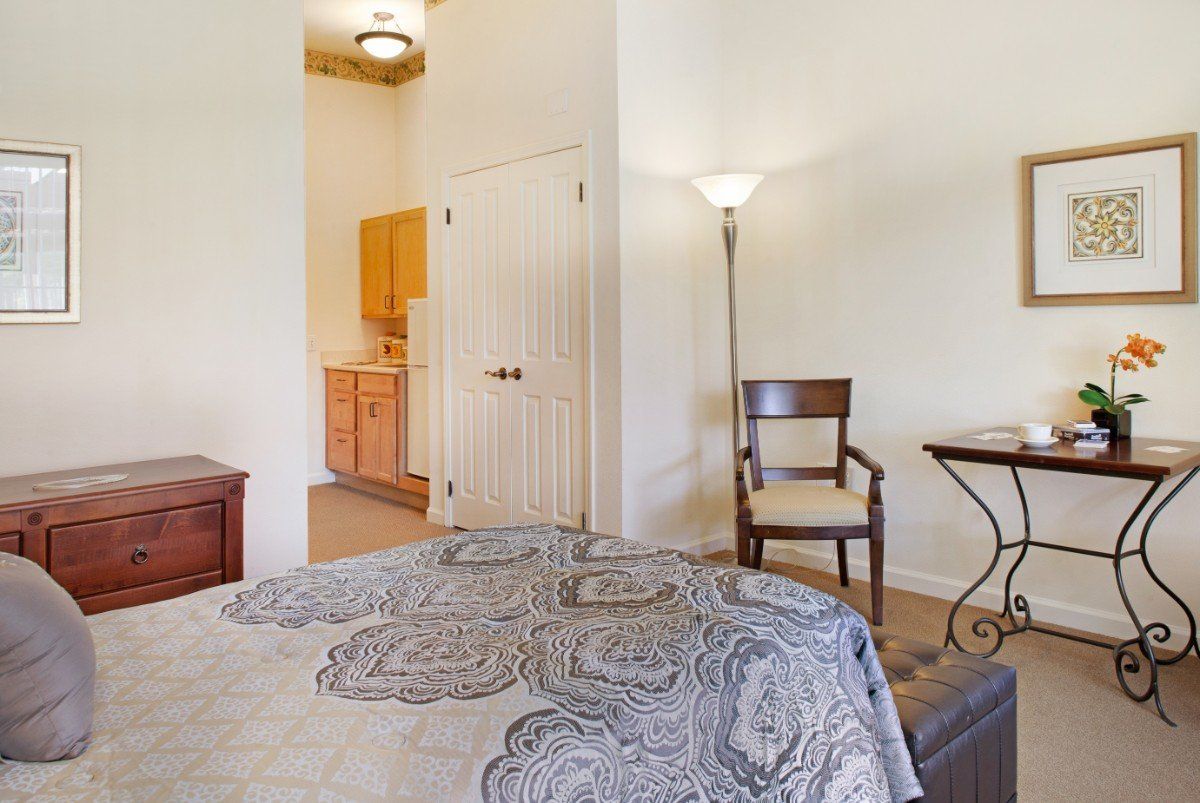 A cozy bedroom with a quilted bedspread, a lamp, and simple furniture.