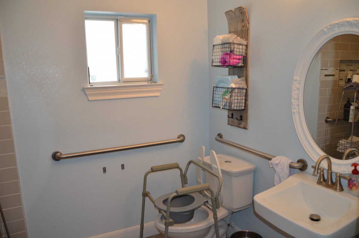 An accessible bathroom equipped with a commode chair and safety grab bars.