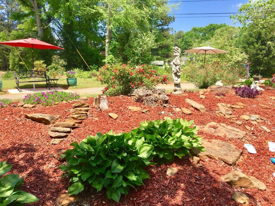 A beautifully landscaped garden featuring lush greenery, stone pathways, and mulch under a sunny sky.